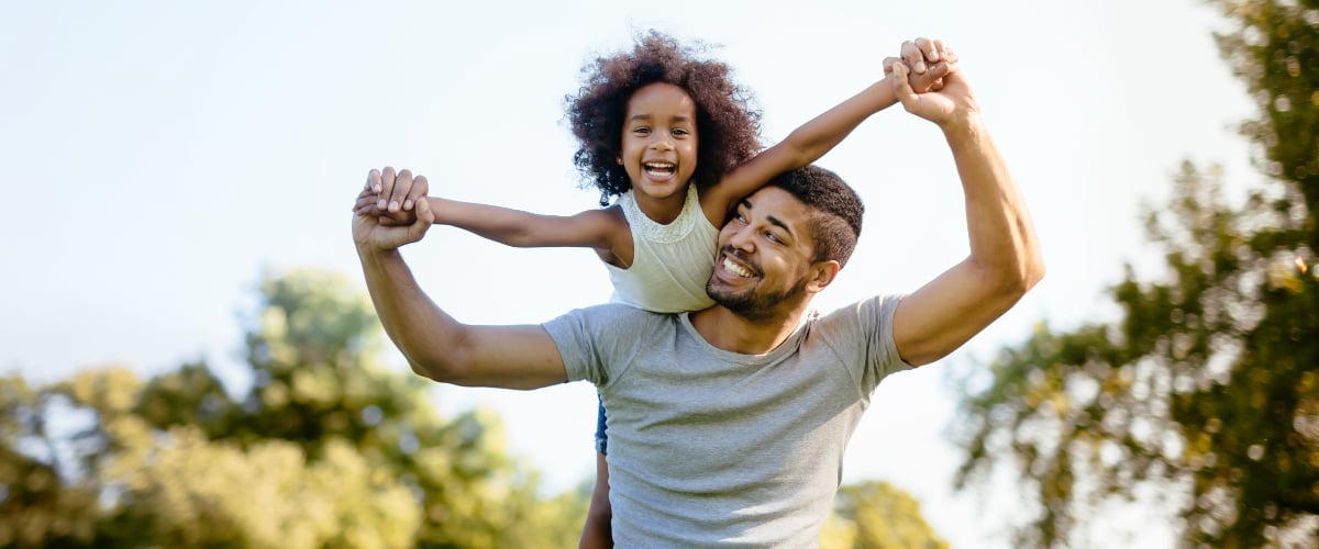 A Black father holds his laughing daughter on his shoulders